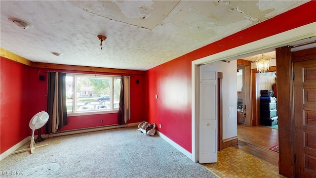 empty room with a notable chandelier, a baseboard radiator, and a textured ceiling