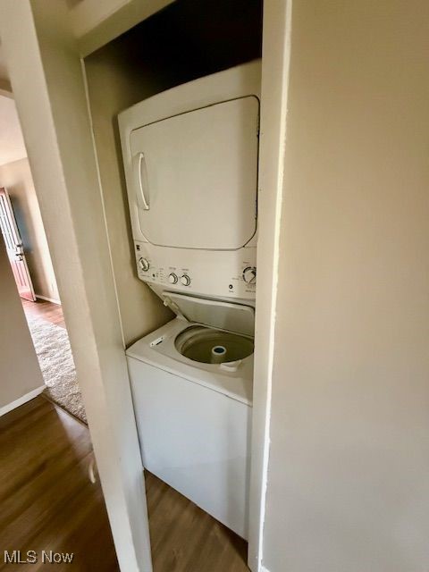 laundry room featuring stacked washer / dryer and dark hardwood / wood-style flooring