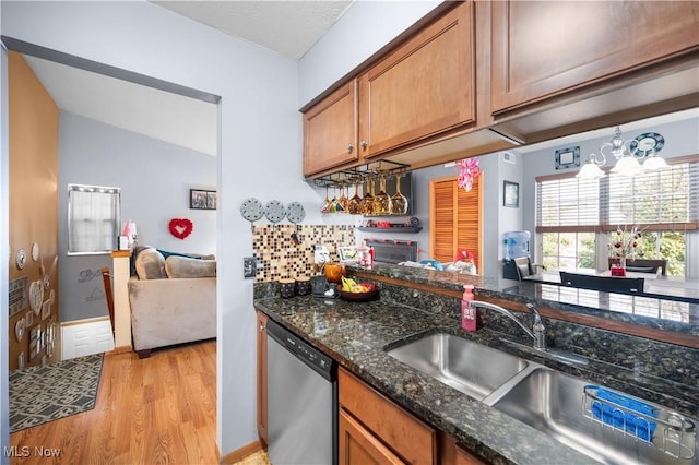 kitchen featuring dishwasher, sink, dark stone countertops, a chandelier, and light wood-type flooring