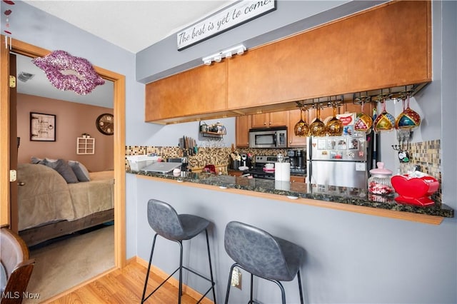 kitchen with tasteful backsplash, dark stone countertops, a kitchen breakfast bar, light hardwood / wood-style floors, and stainless steel appliances