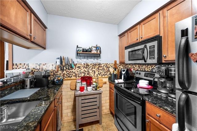 kitchen featuring sink, dark stone counters, a textured ceiling, and appliances with stainless steel finishes