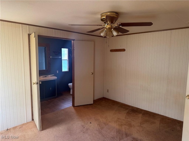 unfurnished bedroom featuring ensuite bath, ornamental molding, ceiling fan, and carpet flooring