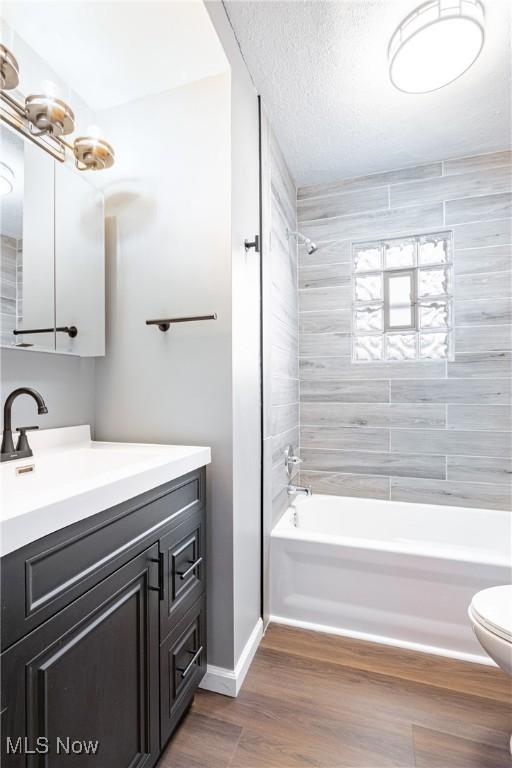 full bathroom with hardwood / wood-style flooring, tiled shower / bath combo, vanity, a textured ceiling, and toilet