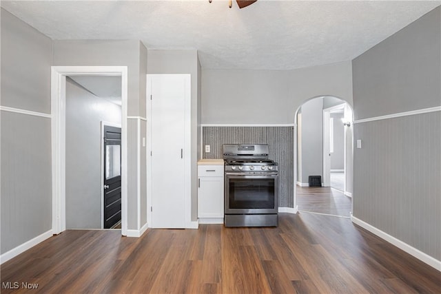 kitchen featuring dark wood-type flooring, ceiling fan, stainless steel gas stove, a textured ceiling, and white cabinets