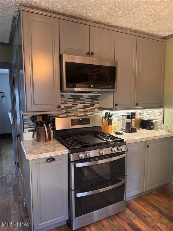 kitchen featuring appliances with stainless steel finishes, gray cabinetry, backsplash, dark hardwood / wood-style floors, and a textured ceiling