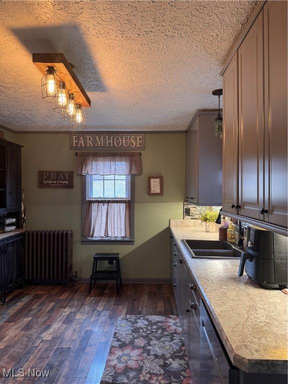 kitchen featuring radiator heating unit, sink, dark hardwood / wood-style flooring, stainless steel dishwasher, and a textured ceiling