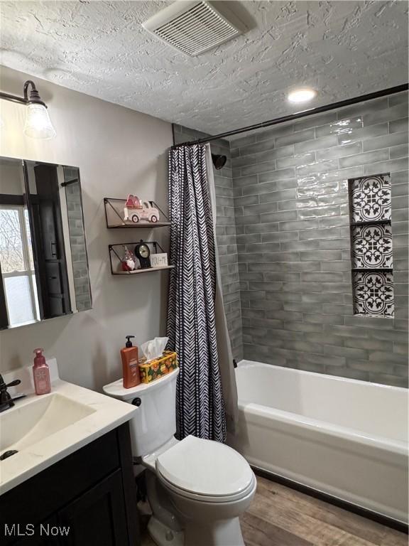 full bathroom featuring shower / bath combination with curtain, hardwood / wood-style flooring, vanity, toilet, and a textured ceiling