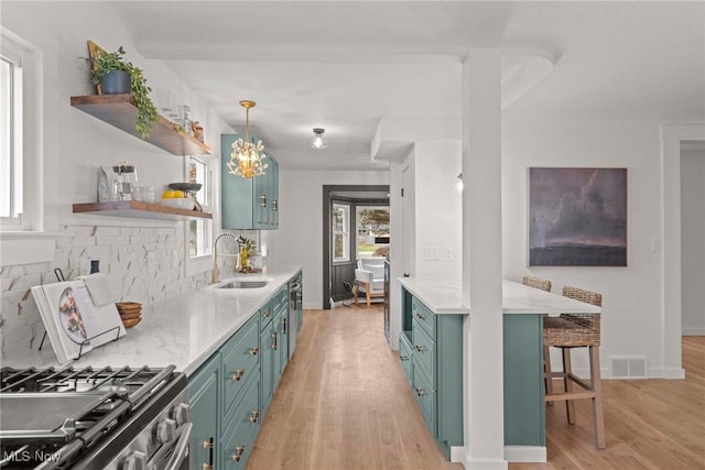 kitchen with stainless steel gas range, sink, decorative light fixtures, light wood-type flooring, and backsplash