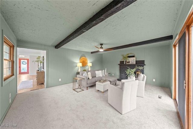 living room featuring a fireplace, beam ceiling, light carpet, and a textured ceiling