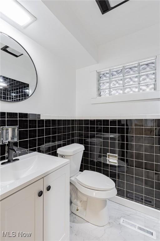 bathroom with vanity, toilet, and tile walls