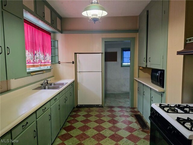 kitchen featuring sink, range hood, gas stove, green cabinetry, and white fridge