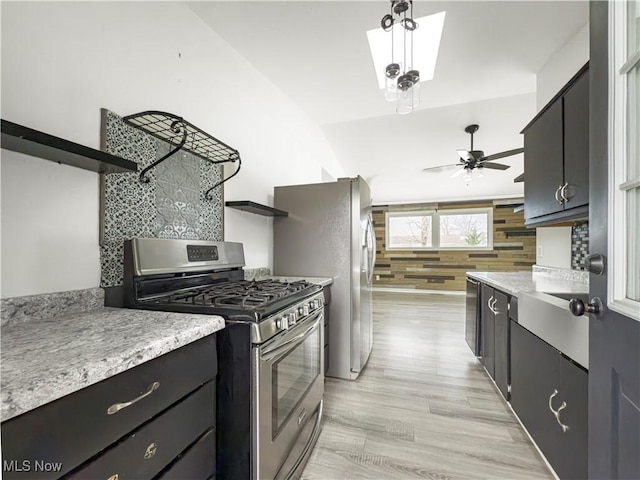 kitchen featuring wooden walls, lofted ceiling, ceiling fan, stainless steel appliances, and light hardwood / wood-style flooring