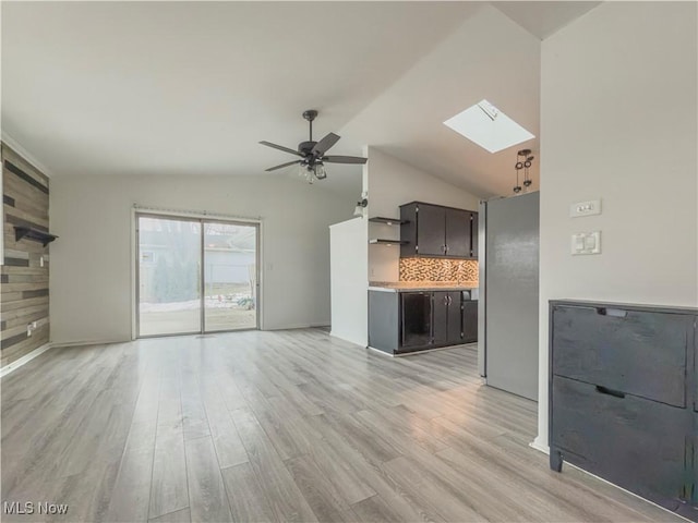 unfurnished living room featuring ceiling fan, wooden walls, light hardwood / wood-style floors, and vaulted ceiling with skylight