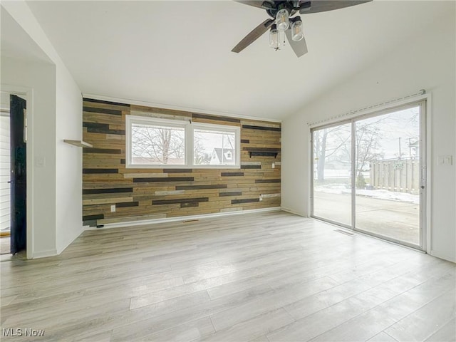 unfurnished room with lofted ceiling, wooden walls, and light hardwood / wood-style flooring