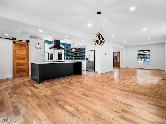 kitchen featuring built in fridge, range hood, hanging light fixtures, a large island, and a barn door