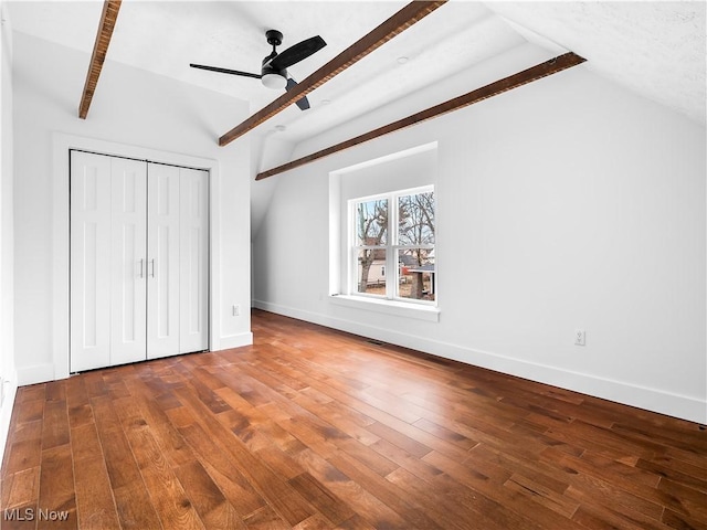 unfurnished bedroom with ceiling fan, hardwood / wood-style floors, a closet, and vaulted ceiling with beams