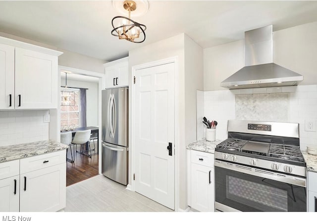 kitchen with appliances with stainless steel finishes, white cabinetry, hanging light fixtures, exhaust hood, and light stone countertops