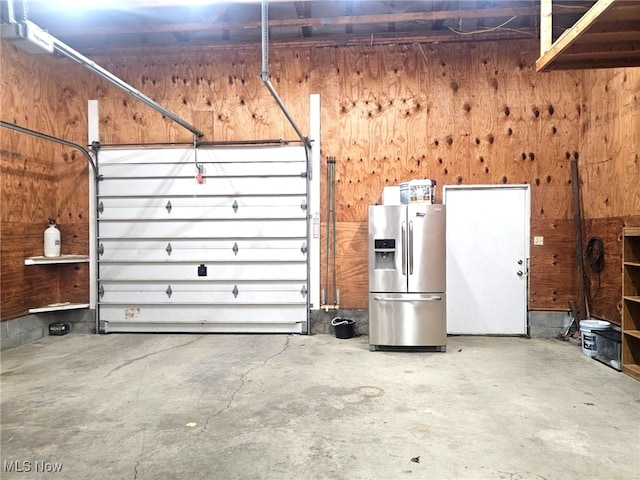 garage featuring stainless steel refrigerator with ice dispenser and wooden walls