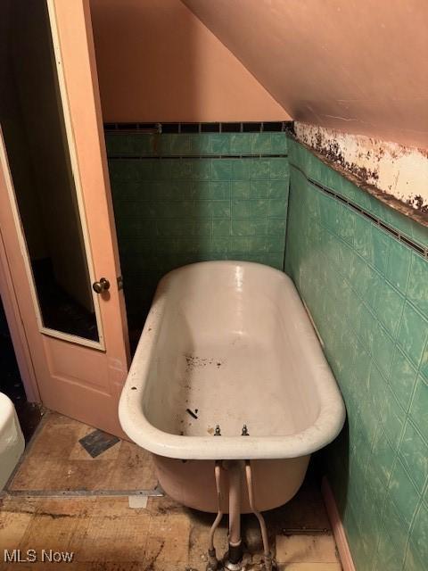 bathroom featuring lofted ceiling, tile walls, and a tub