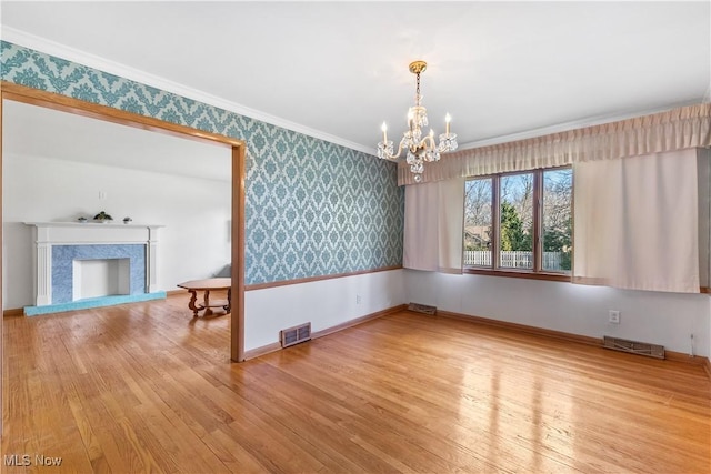 unfurnished room with an inviting chandelier, hardwood / wood-style flooring, ornamental molding, and a premium fireplace