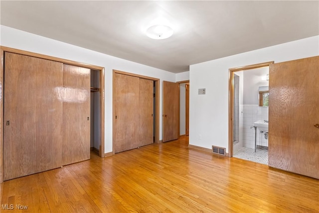 unfurnished bedroom featuring multiple closets, ensuite bath, and light wood-type flooring