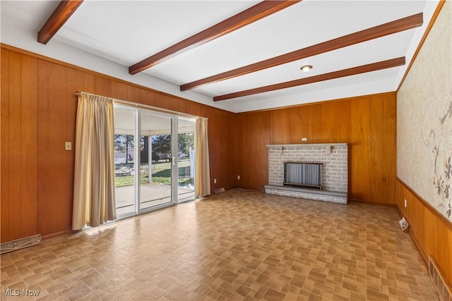 unfurnished living room with a fireplace, beam ceiling, and wood walls