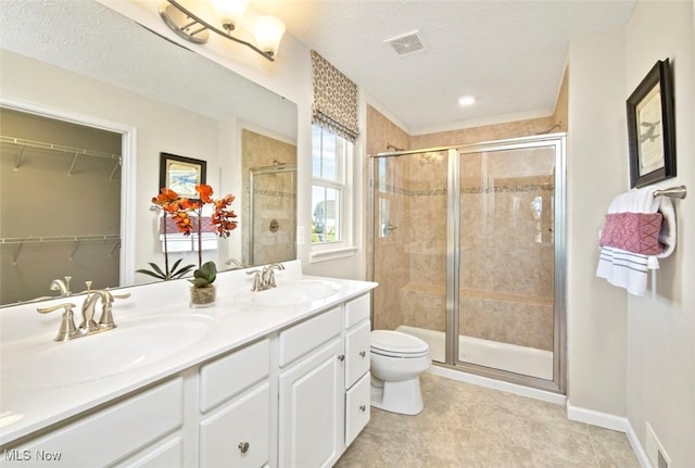 bathroom featuring toilet, vanity, a textured ceiling, and a shower with shower door