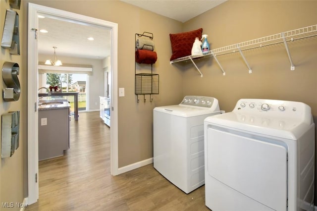 washroom featuring an inviting chandelier, sink, light hardwood / wood-style floors, and washing machine and clothes dryer