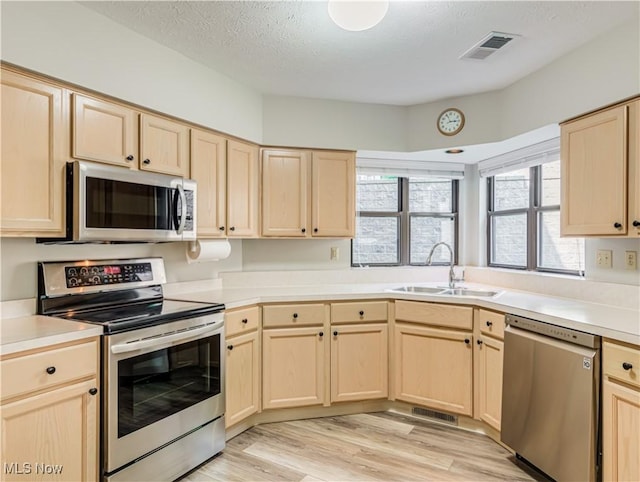 kitchen with appliances with stainless steel finishes, sink, light brown cabinetry, and light hardwood / wood-style flooring