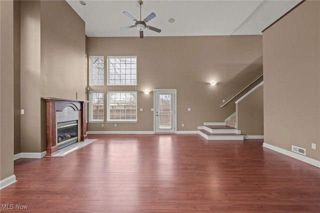 unfurnished living room with ceiling fan, a high end fireplace, wood-type flooring, and a high ceiling