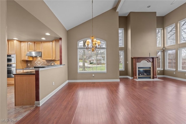 kitchen featuring light brown cabinetry, decorative light fixtures, tasteful backsplash, a premium fireplace, and dark wood-type flooring