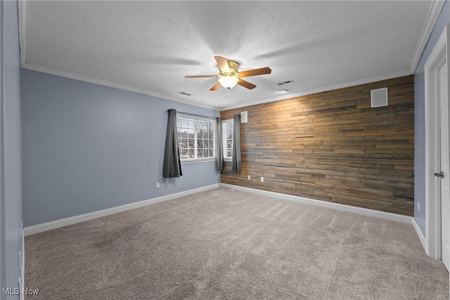 spare room featuring a textured ceiling, ornamental molding, wooden walls, carpet floors, and ceiling fan