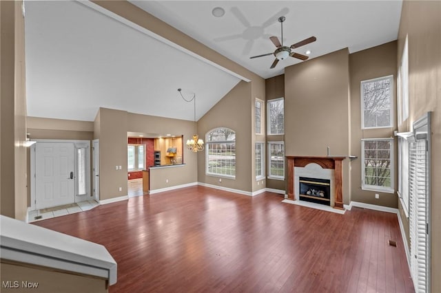 living room with wood-type flooring, high vaulted ceiling, a high end fireplace, beam ceiling, and ceiling fan with notable chandelier