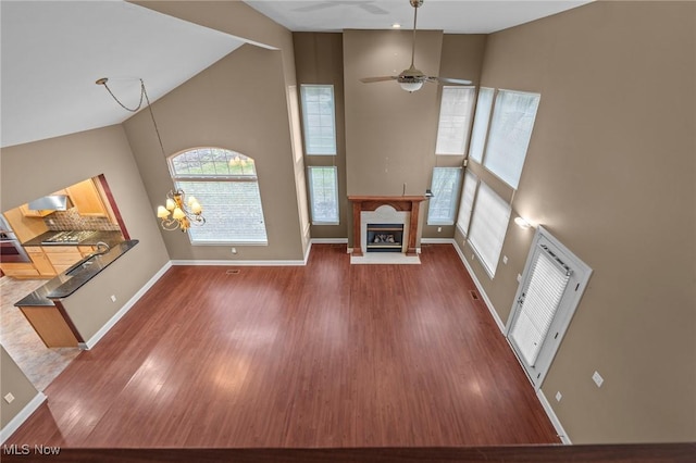 unfurnished living room with dark wood-type flooring, ceiling fan with notable chandelier, and high vaulted ceiling