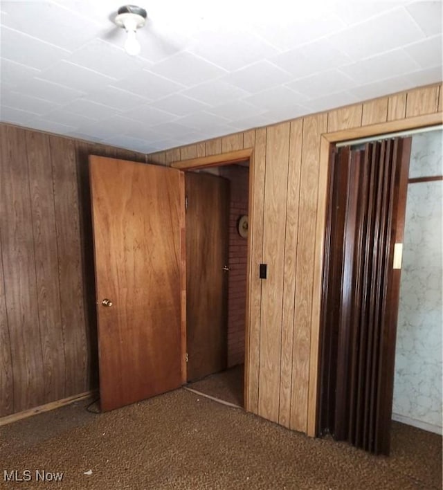 unfurnished bedroom featuring dark colored carpet and wood walls