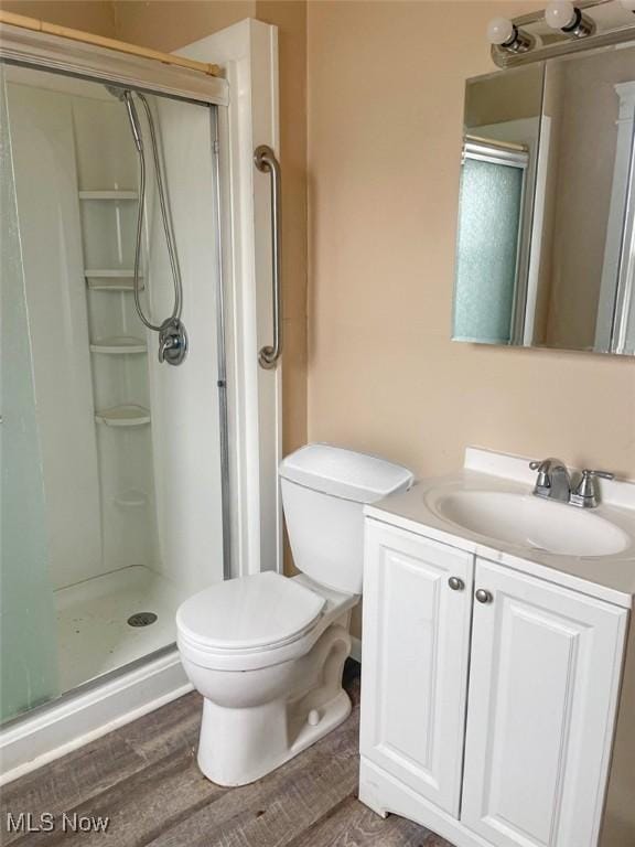 bathroom with toilet, a shower stall, wood finished floors, and vanity