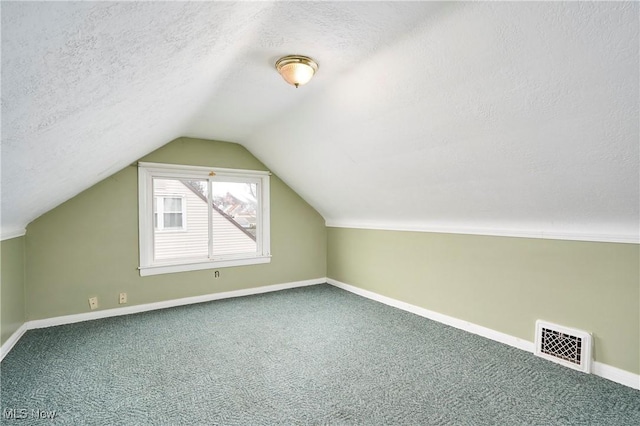 additional living space with vaulted ceiling, a textured ceiling, and carpet flooring