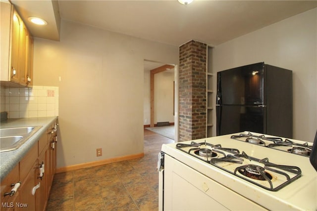 kitchen with black refrigerator, sink, decorative backsplash, and white gas range oven