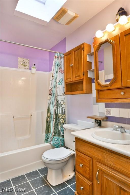 full bathroom with toilet, a skylight, shower / bath combo, tile patterned flooring, and backsplash