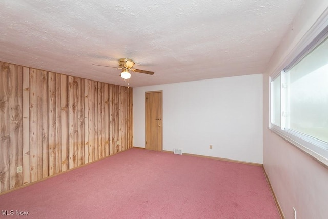 carpeted empty room featuring ceiling fan, a textured ceiling, and wood walls