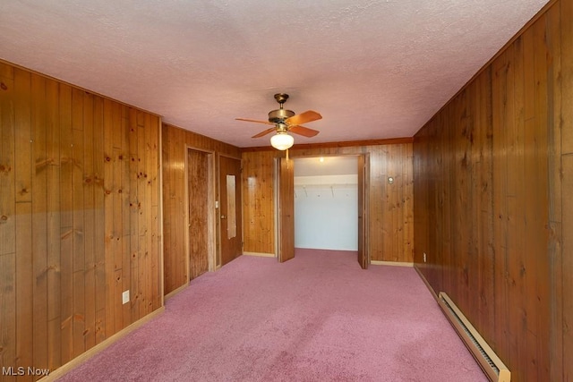 unfurnished room with a baseboard heating unit, light colored carpet, a textured ceiling, and wood walls