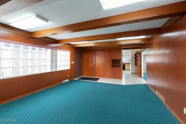 carpeted spare room with beamed ceiling and wood walls