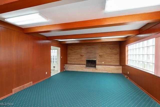 unfurnished living room featuring a brick fireplace, wooden walls, beamed ceiling, and carpet flooring