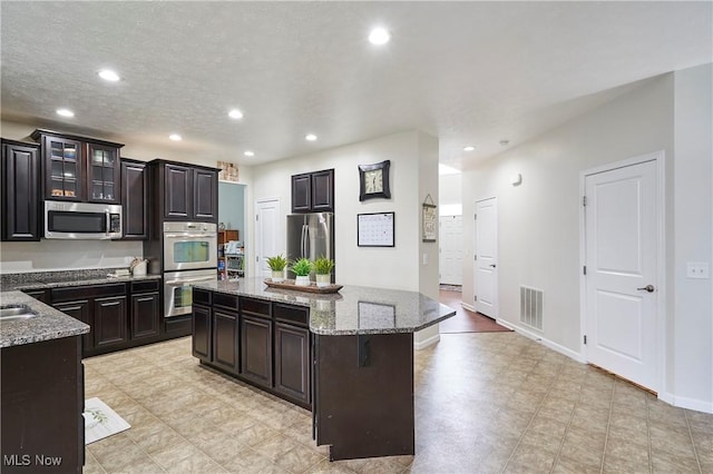 kitchen with a kitchen bar, light stone counters, a center island, dark brown cabinets, and appliances with stainless steel finishes