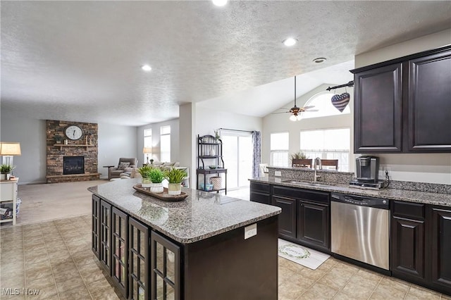 kitchen featuring a stone fireplace, sink, a center island, stainless steel dishwasher, and light stone counters