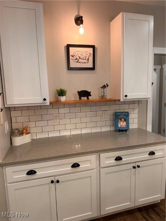 interior space featuring white cabinetry, dark wood-type flooring, light stone counters, and decorative backsplash