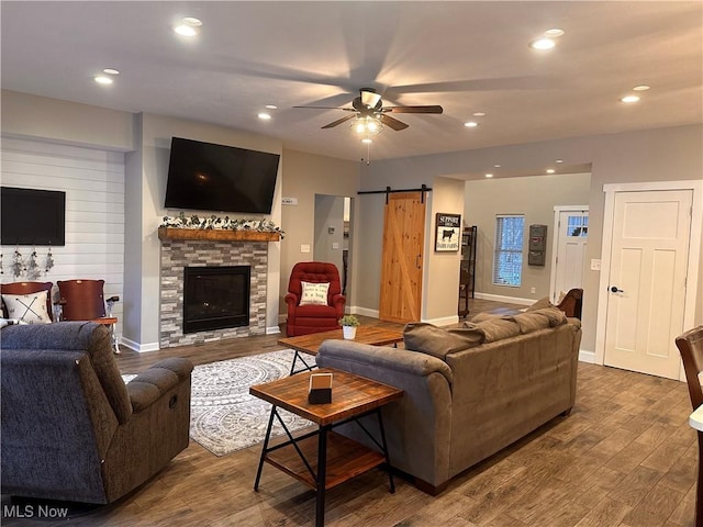 living room with a fireplace, dark wood-type flooring, a barn door, and ceiling fan