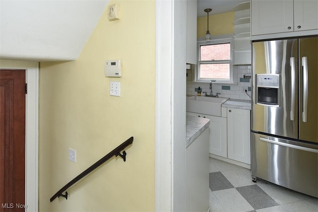 kitchen with pendant lighting, sink, white cabinets, stainless steel fridge, and decorative backsplash