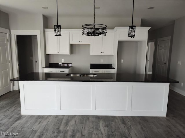 kitchen with dark countertops, dark wood-style floors, a center island, white cabinets, and baseboards