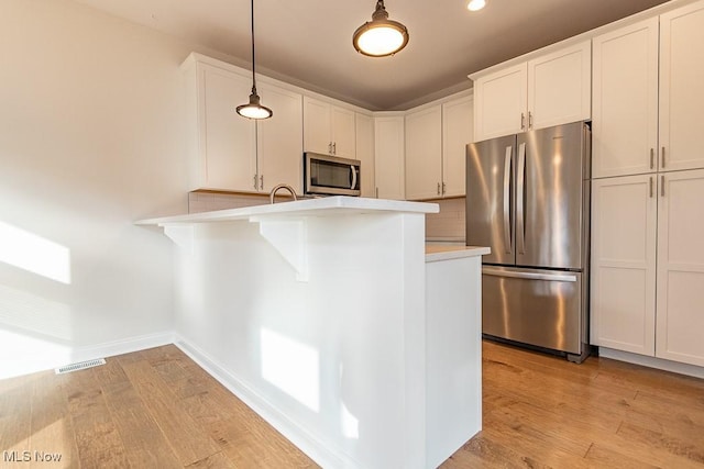 kitchen with white cabinets, hanging light fixtures, kitchen peninsula, stainless steel appliances, and light hardwood / wood-style flooring